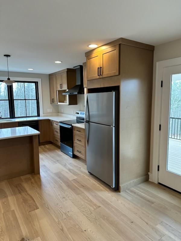 Modern kitchen featuring stainless steel refrigerator, wood cabinets, light hardwood floors, and a kitchen island.