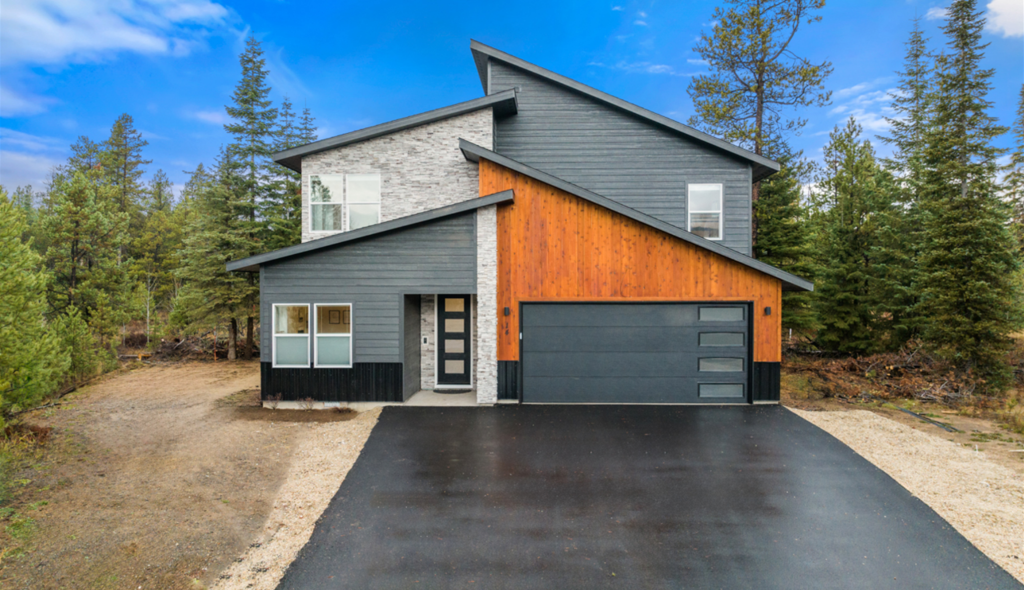 A modern house with a garage and a driveway is surrounded by trees.