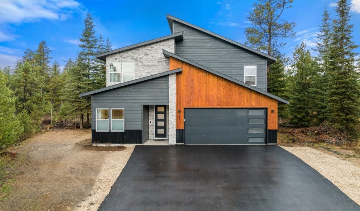 A modern house with a garage and a driveway is surrounded by trees.