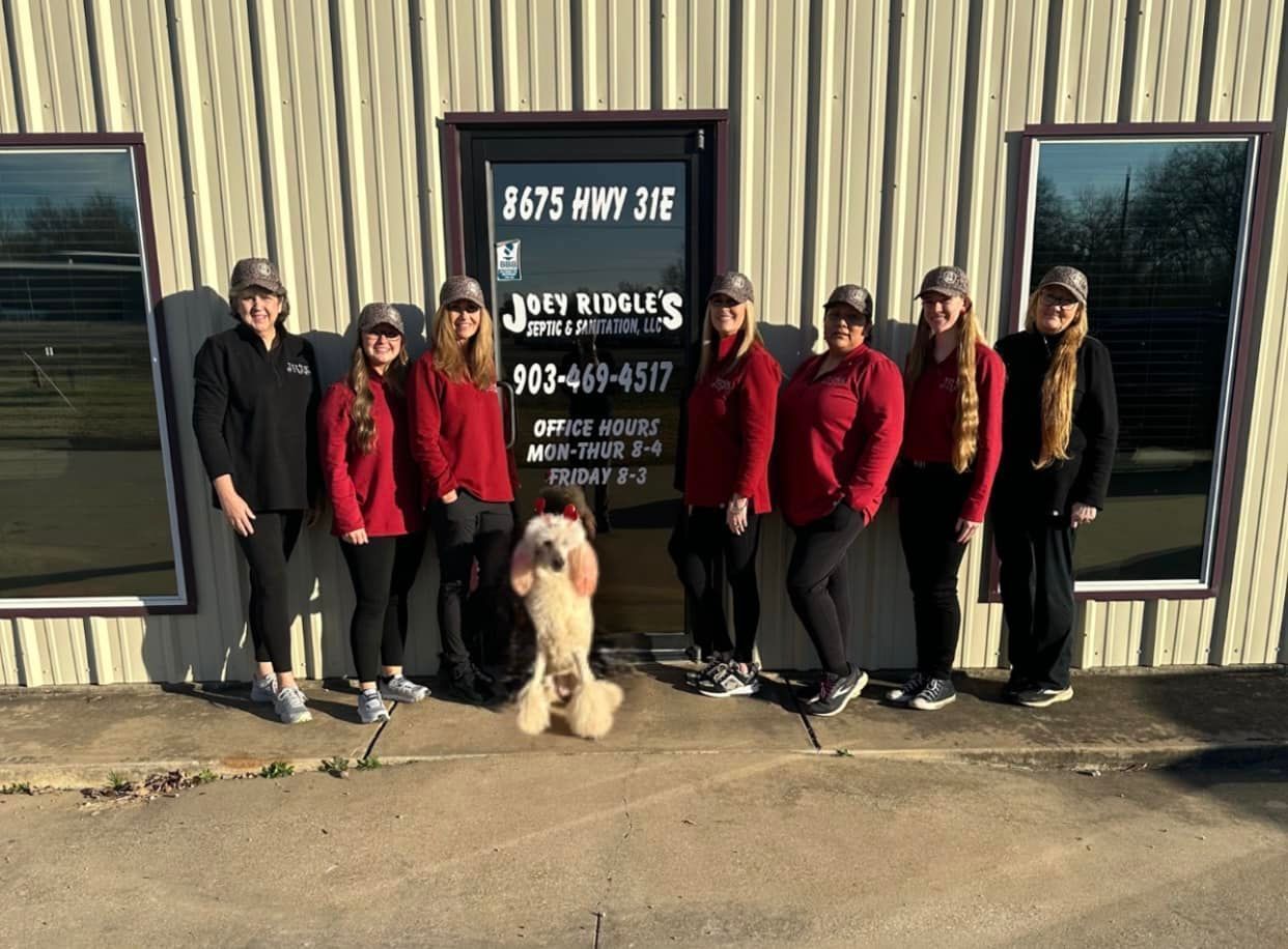 Group of people in red shirts and hats with a dog standing outside a business.