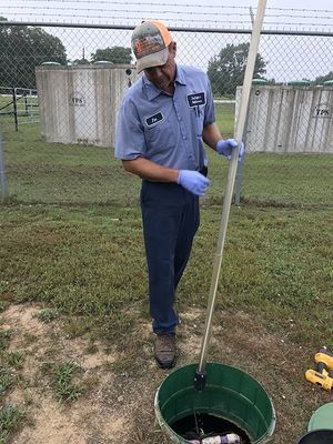 Man in blue work clothes taking a sample from a well, outdoors.