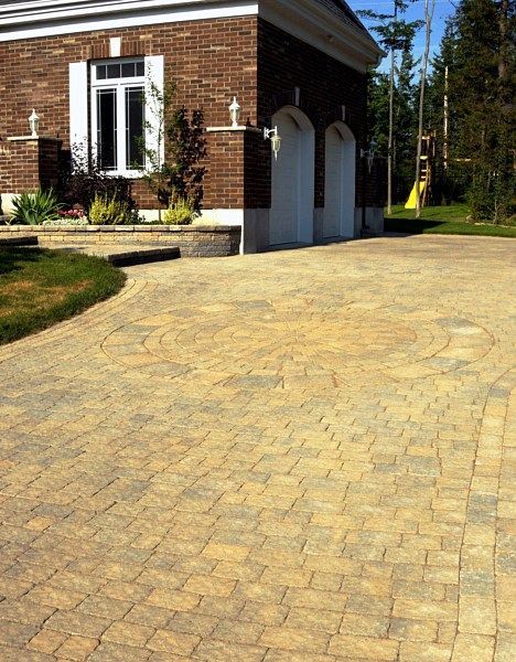 A brick house with a garage and a beige, patterned stone paver driveway under a sunny sky.