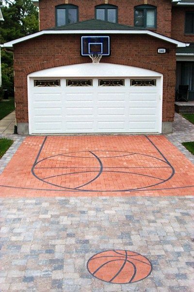 A residential brick garage with a mounted basketball hoop over a driveway paved to look like a basketball court.