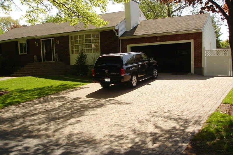 A single-story brick house with a paved driveway, open garage, and a black SUV parked in front.