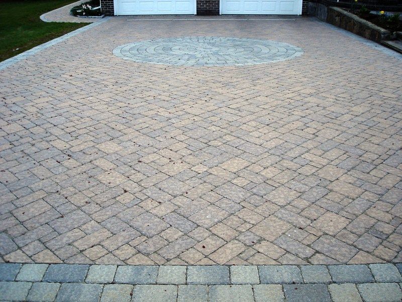 A paved driveway made of multi-colored rectangular stone blocks in a diamond pattern, featuring a central circular design.