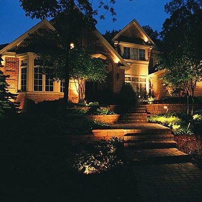 A brick house at twilight featuring warm exterior landscape lighting illuminating the stone stairs and surrounding trees.
