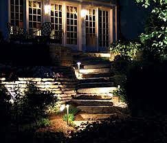 An outdoor stone staircase illuminated at night by small path lights, leading up to a house with glowing French doors.