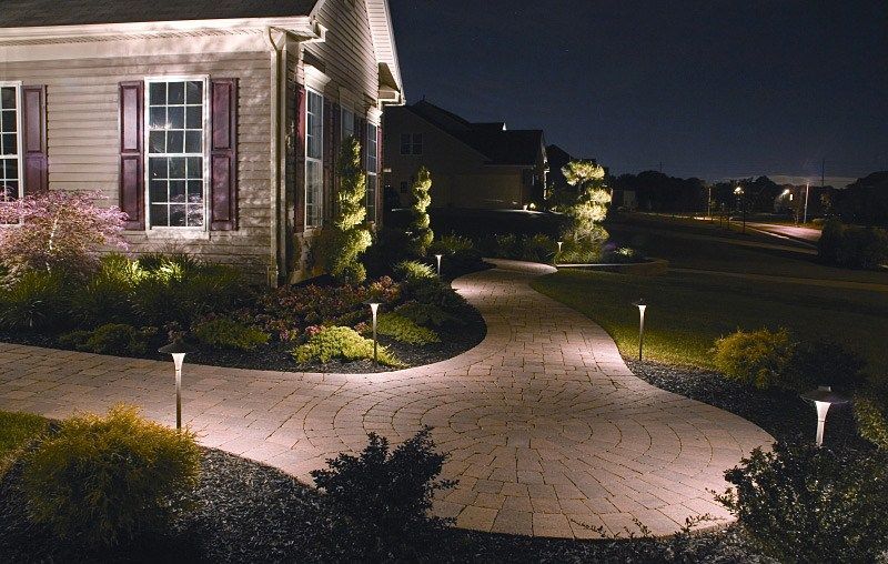 A residential walkway at night, illuminated by small solar path lights beside landscaped garden beds.