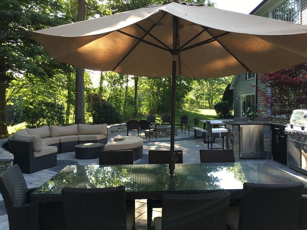 A patio featuring a glass-topped dining table with an umbrella, wicker chairs, and a curved sectional sofa in a yard.
