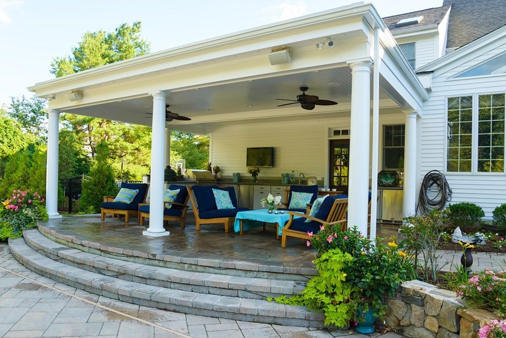 A covered outdoor patio featuring comfortable blue seating and stone stairs, attached to a white suburban home.