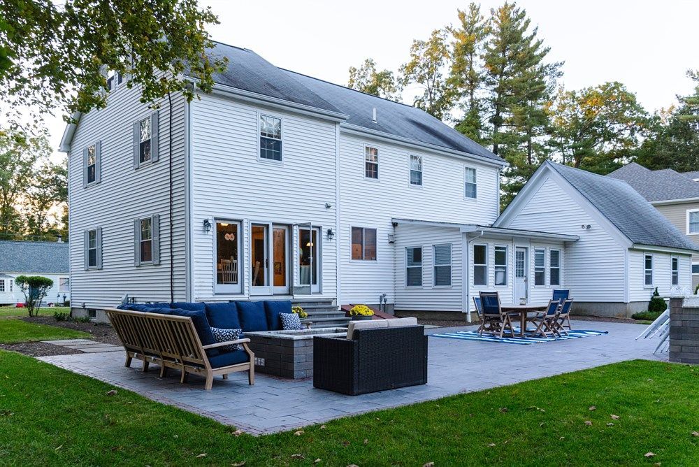 Backyard patio with outdoor furniture and a fire pit attached to a two-story white house with siding and a sunroom.