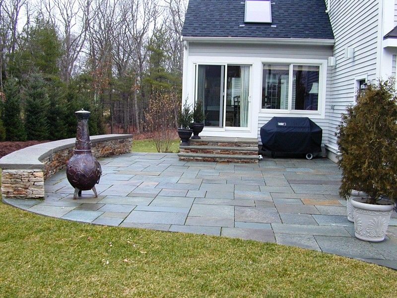 A stone patio with a curved seating wall, a fire pit, and steps leading to a house with sliding glass doors.