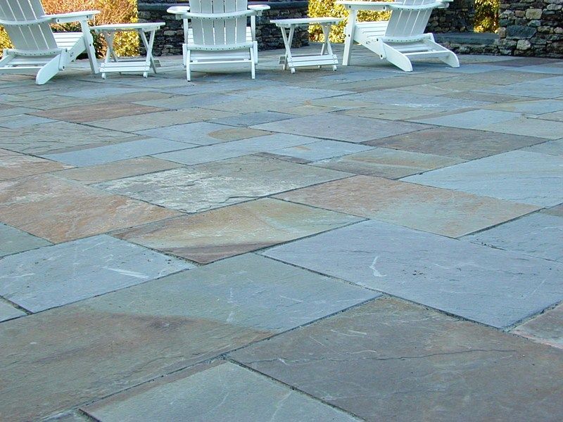 White Adirondack chairs and side tables on a gray and tan stone patio.
