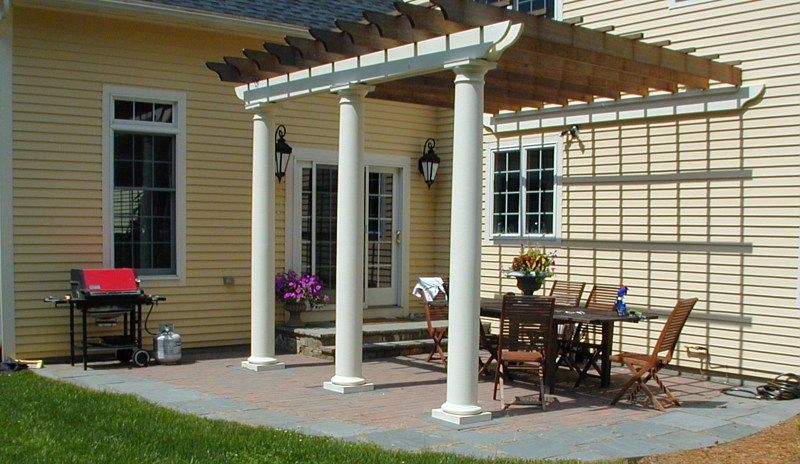 A yellow house with a patio featuring a pergola, outdoor dining furniture, and a grill on a sunny day.