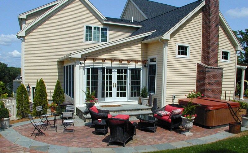 A yellow house with a patio featuring a hot tub, outdoor furniture, and a pergola over the glass-paned doors.