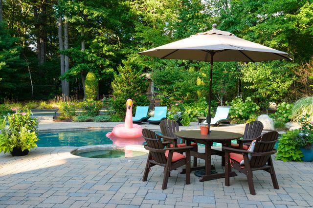 Backyard patio with table, chairs, umbrella, and pink flamingo float beside a pool