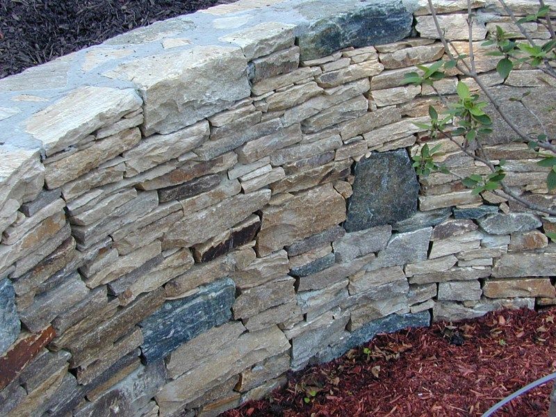 A curved, dry-stacked stone retaining wall made of layered, multi-colored natural fieldstone.