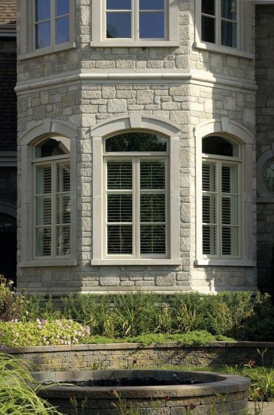 A stone bay window tower on a building exterior with light-colored trim and a small garden in the foreground.