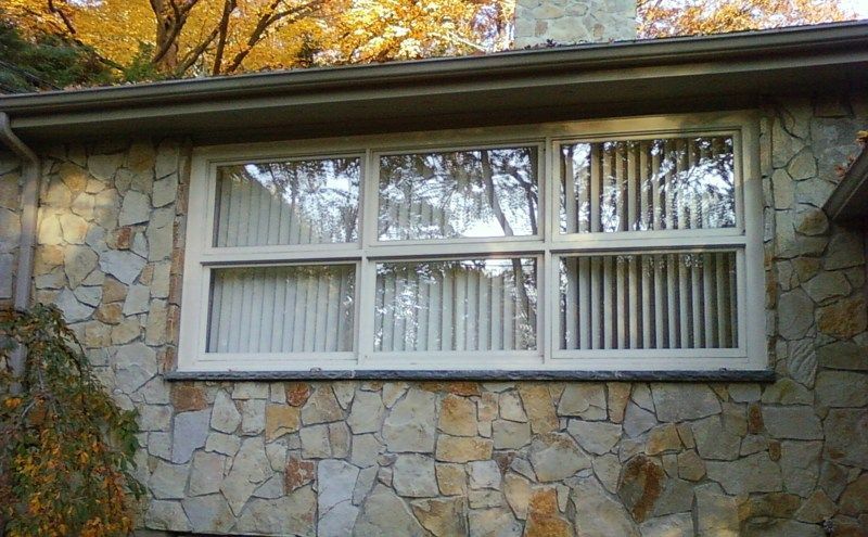 A wide, multi-paned window with white frames set into a textured, light-colored stone wall under an eave.