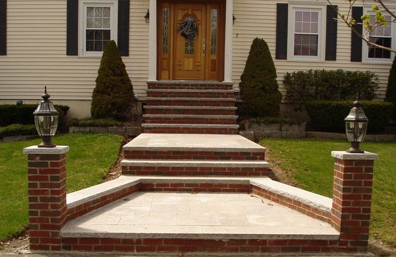 Front-facing view of a brick house entrance with a tiered brick and stone walkway leading to wooden front doors.