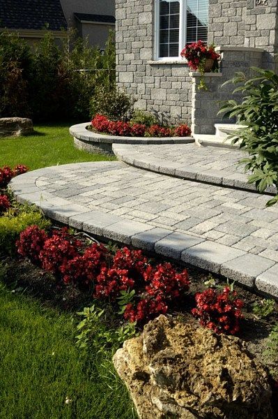 Stone steps and a paved patio area leading to a house entrance, accented by vibrant red flowers and a textured garden rock.