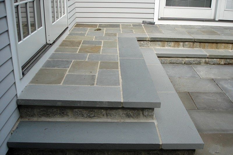 A stone patio landing with two steps, featuring a mix of rectangular pavers and smooth, grey stone slab treads.