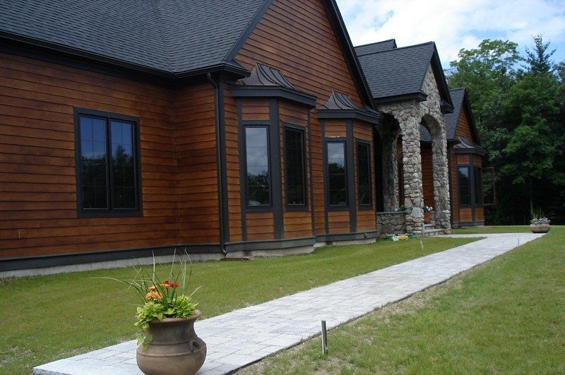 A wood-paneled house with dark roofing and stone accents features a stone walkway leading to an arched entrance.