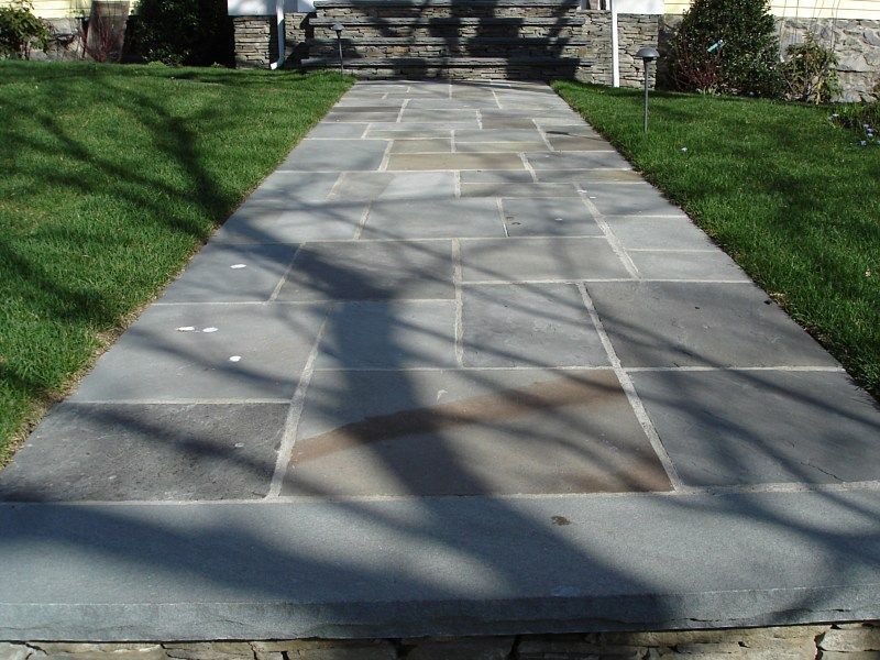 A stone walkway made of large, rectangular gray pavers leads from the foreground to the steps of a building.