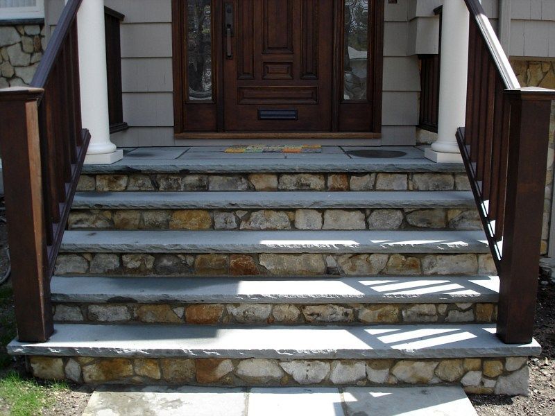 Front entrance with four stone steps featuring slate treads and fieldstone risers, flanked by wooden railings and columns.