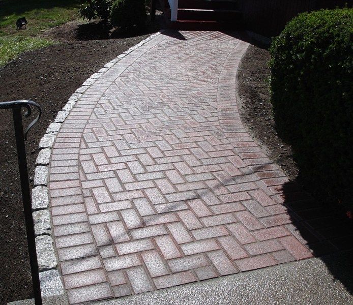 A curved brick walkway in a herringbone pattern with a granite stone border, leading to a home entryway.