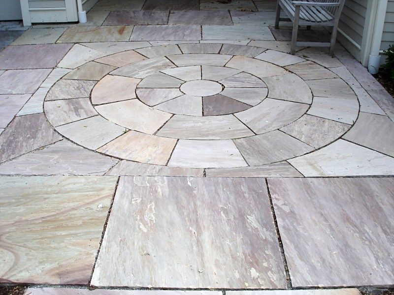 A circular stone patio feature built into a square-tiled stone walkway in neutral tan and beige tones.