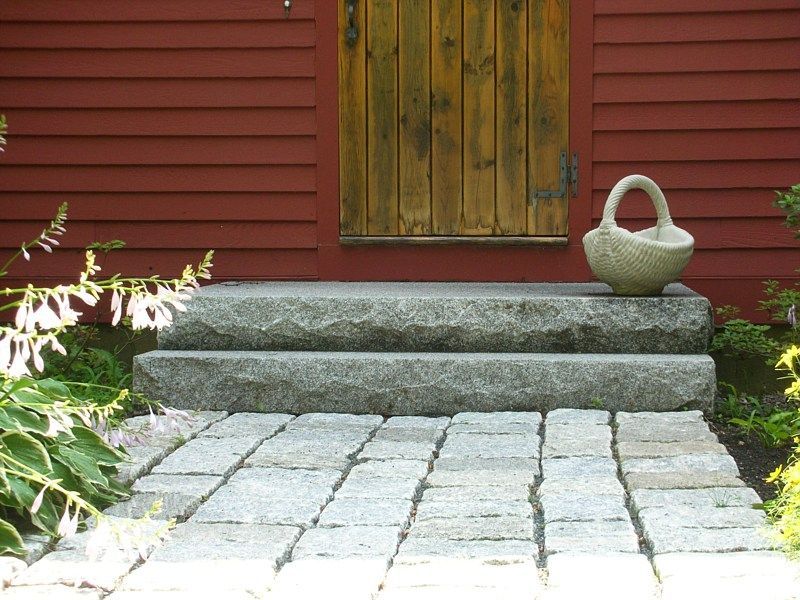 Stone steps lead to a wooden door on a house with red siding, featuring a stone path and a decorative basket.