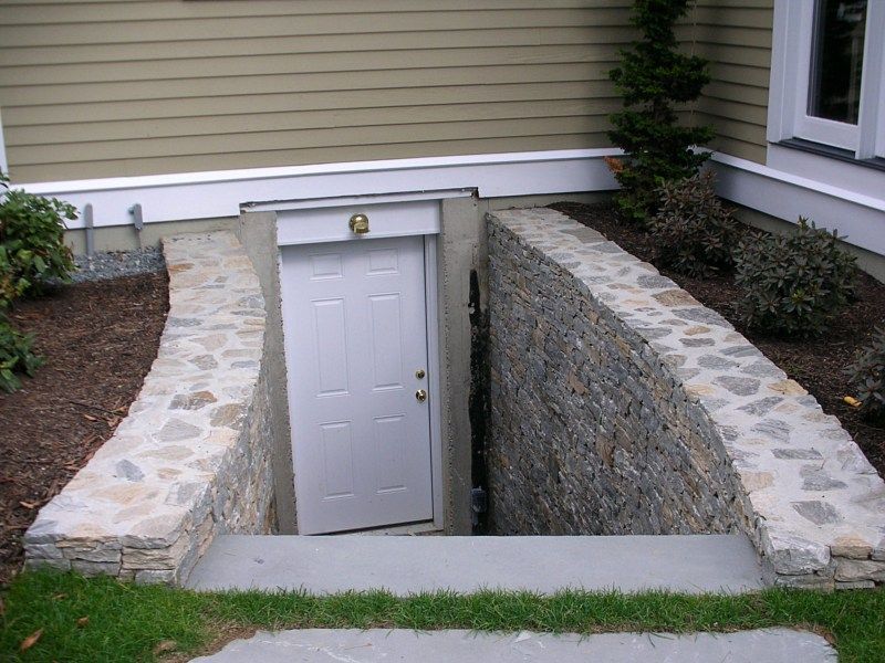 A white door at the base of stone steps leading into a basement entrance on the side of a house.
