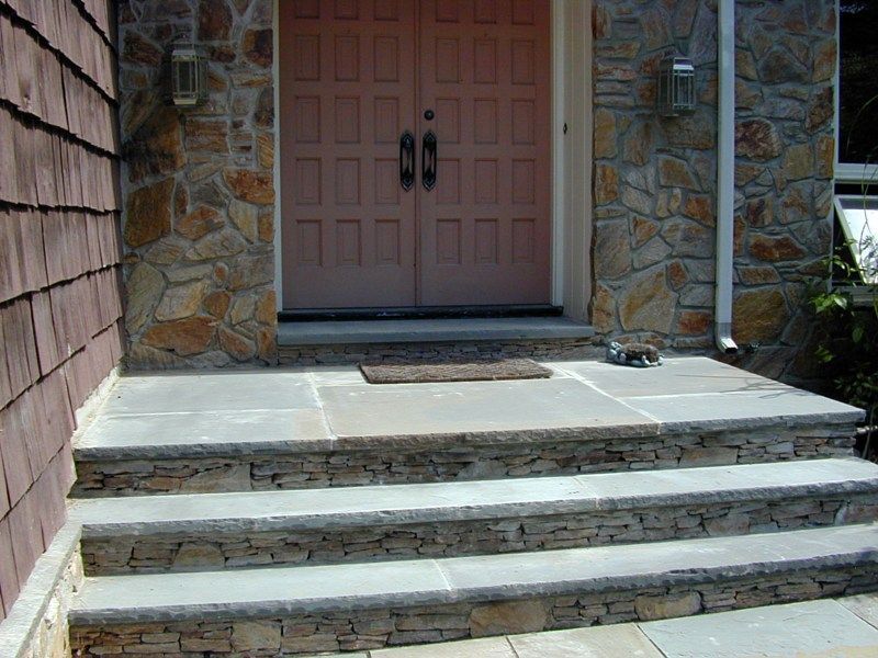 Three stone steps leading up to a landing with a brown double door and stone siding exterior.