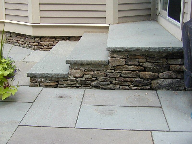 Stone steps with gray slab treads leading up to a house door, with a matching stone patio in the foreground.