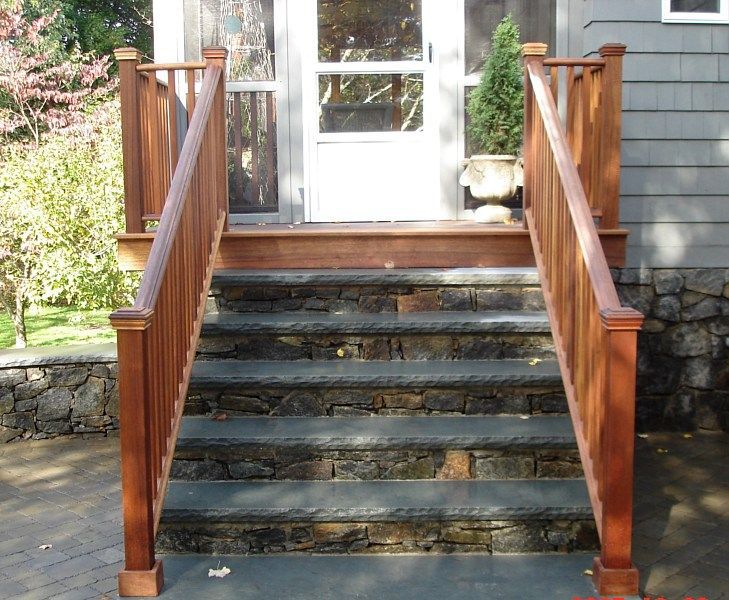 Stone steps with a landing and wooden railings leading up to a screen door on a grey house.