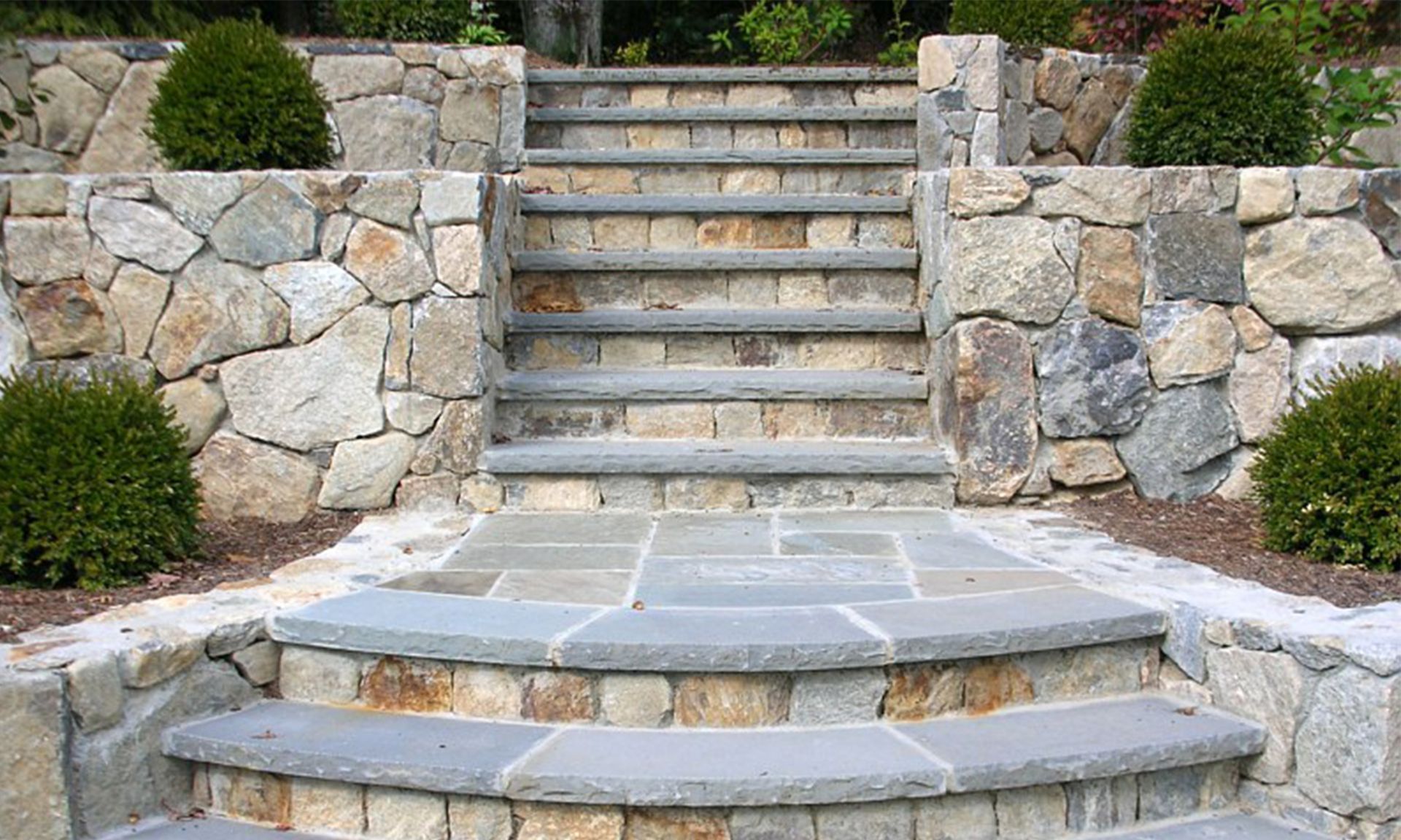 Stone steps and retaining walls leading to a landscaped garden path with shrubs.
