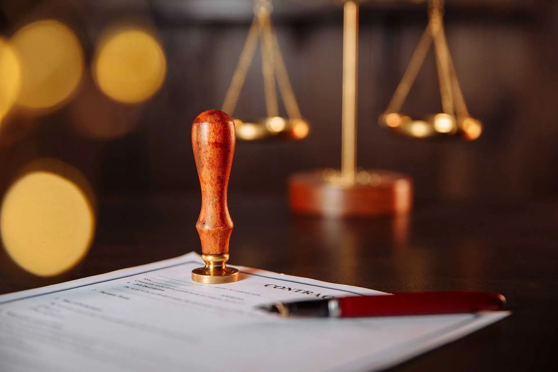Scales of justice, notary stamp, and pen on legal document, dark setting with bokeh lights.