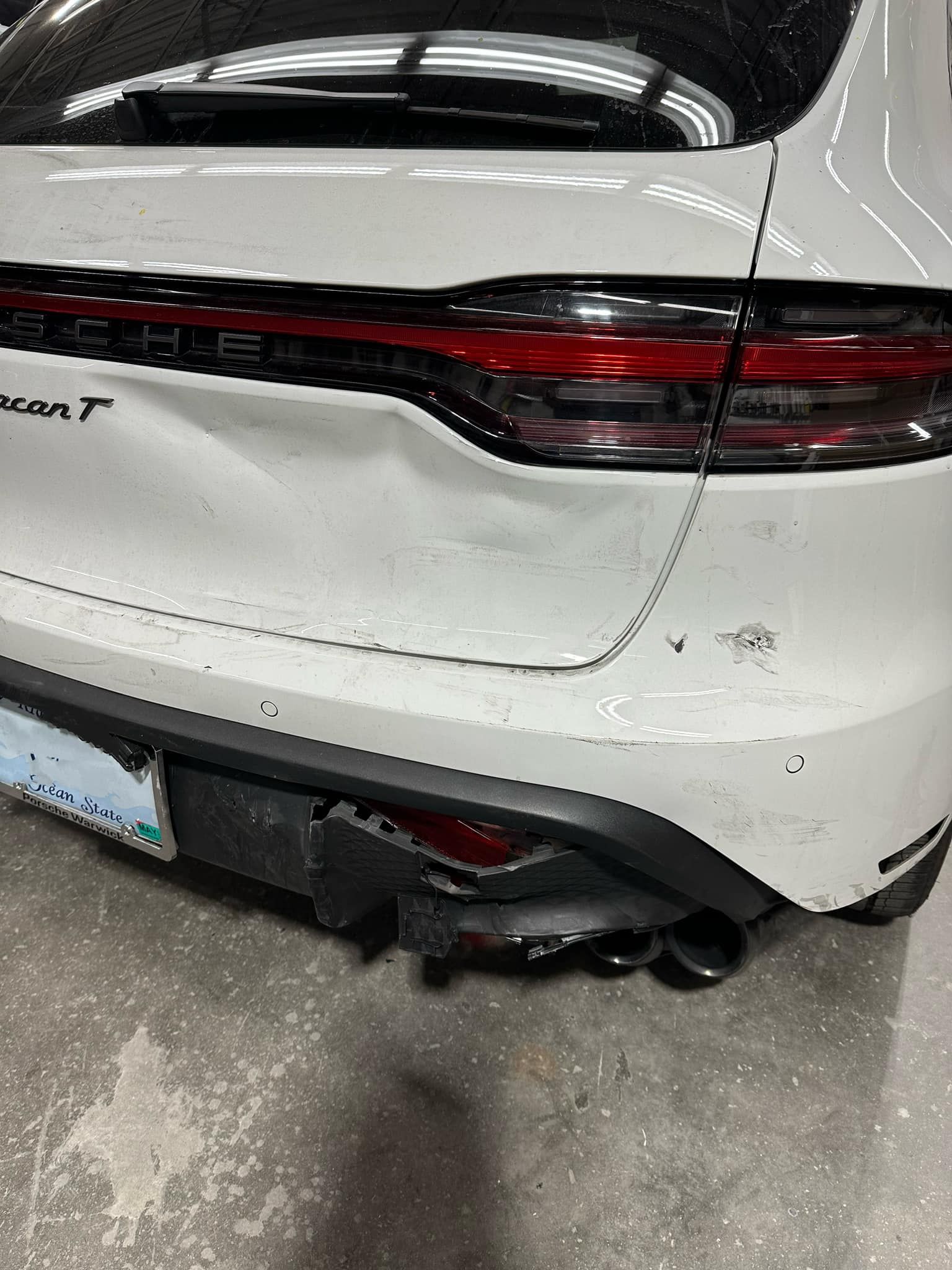 A white car with a damaged rear bumper is parked in a garage.