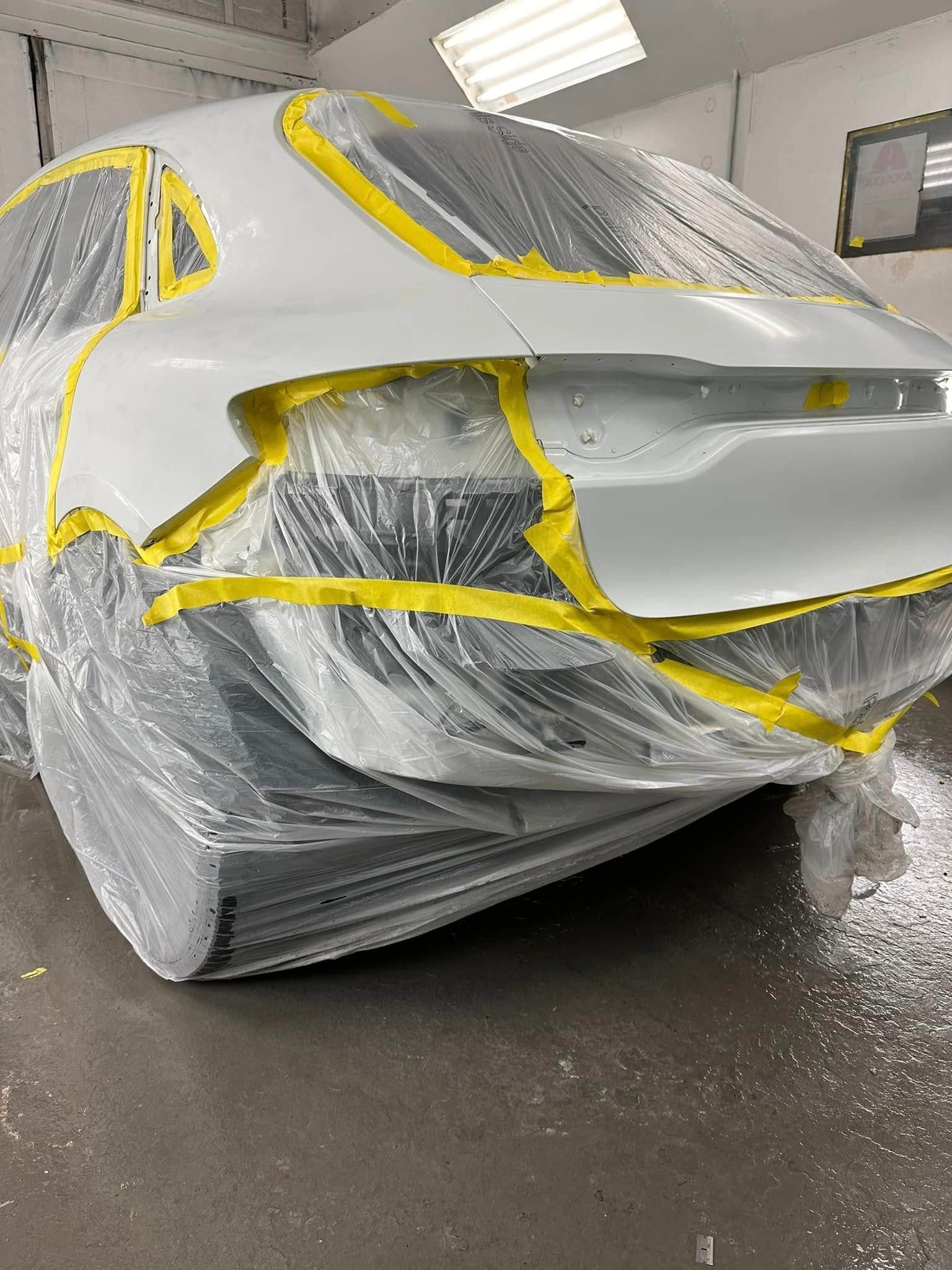 A white car is covered in plastic and yellow tape in a garage.