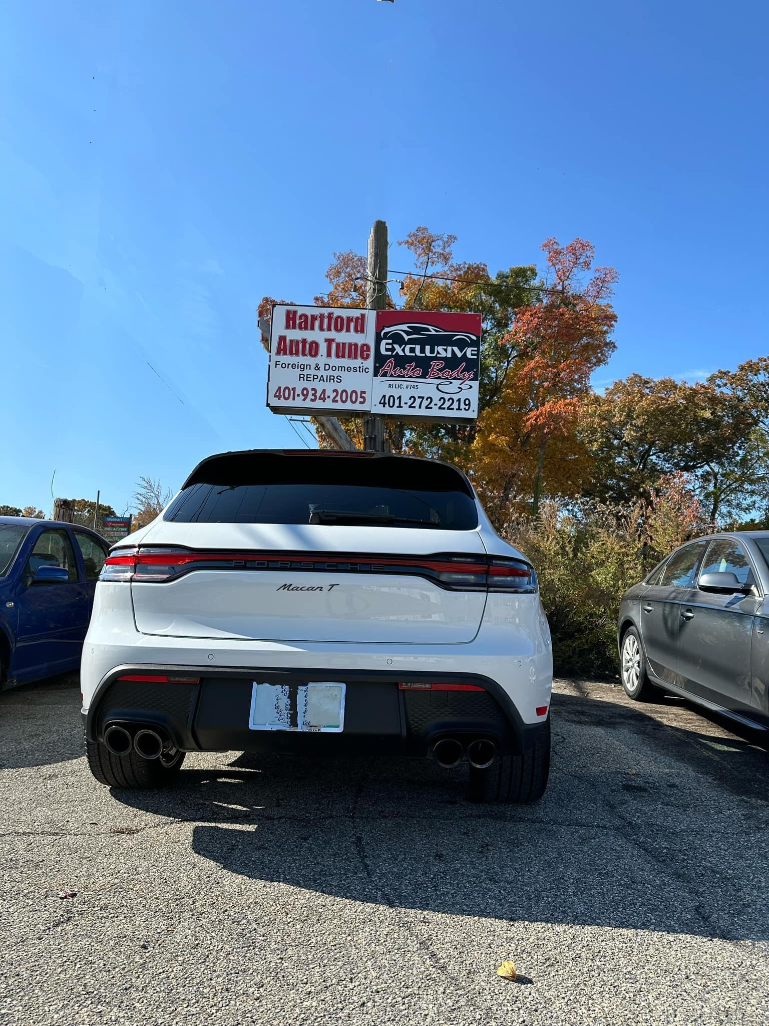A white car is parked in a gravel lot with a sign above it.