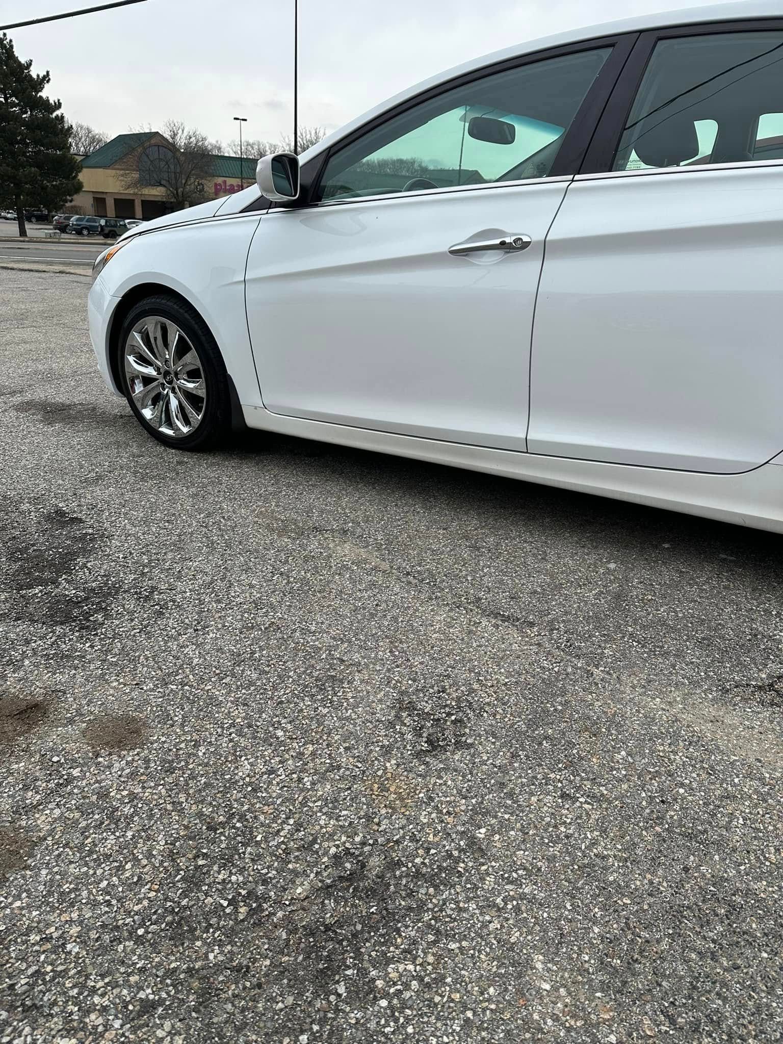 A white car is parked in a gravel lot.