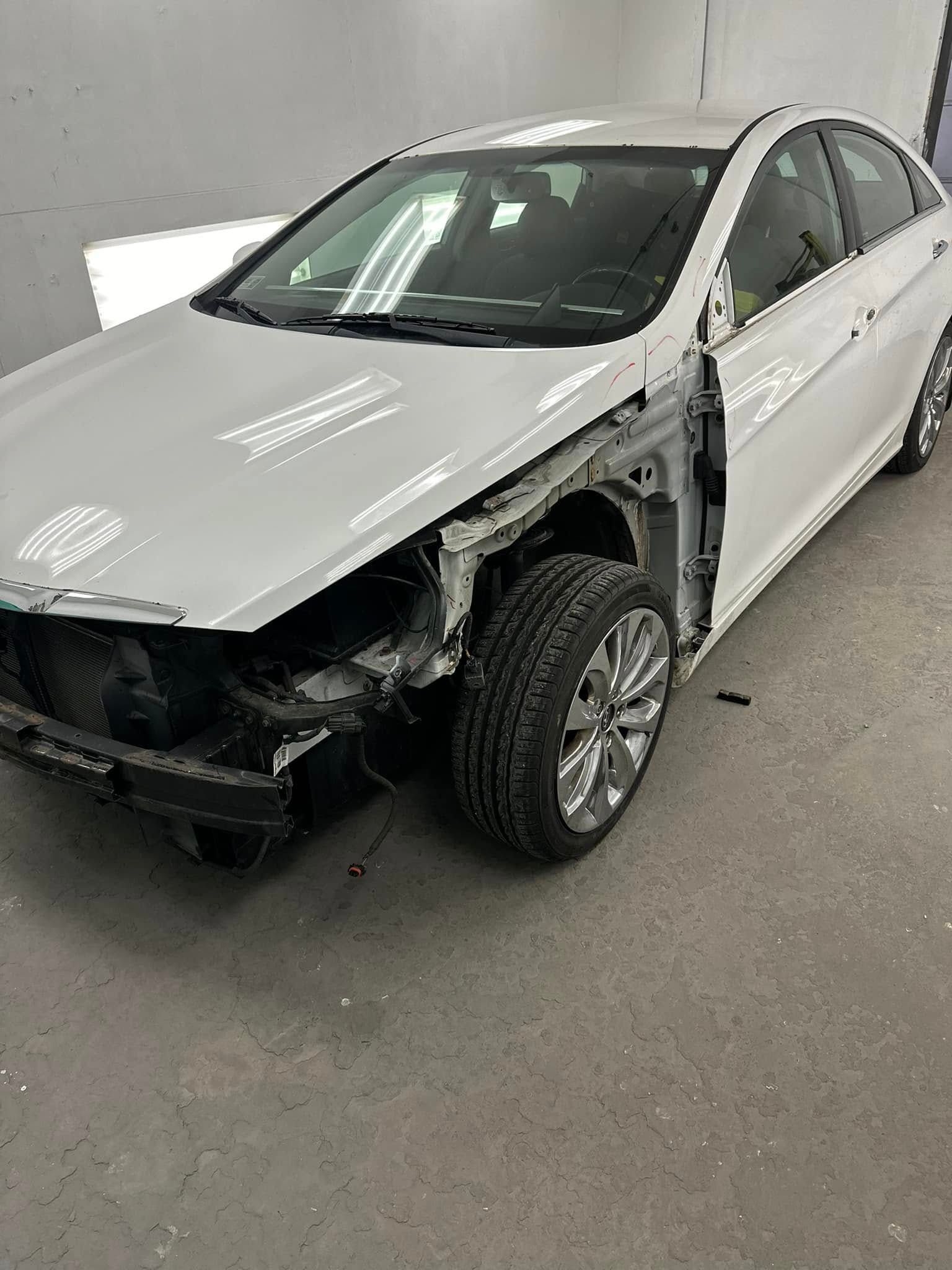 A white car with a damaged hood is sitting in a garage.