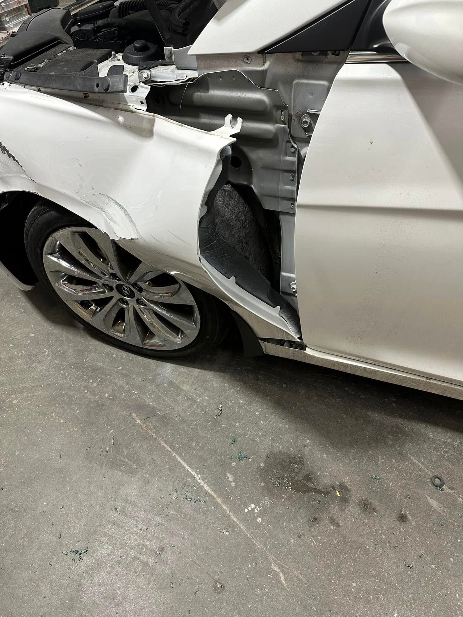 A white car with a damaged fender is parked in a garage.
