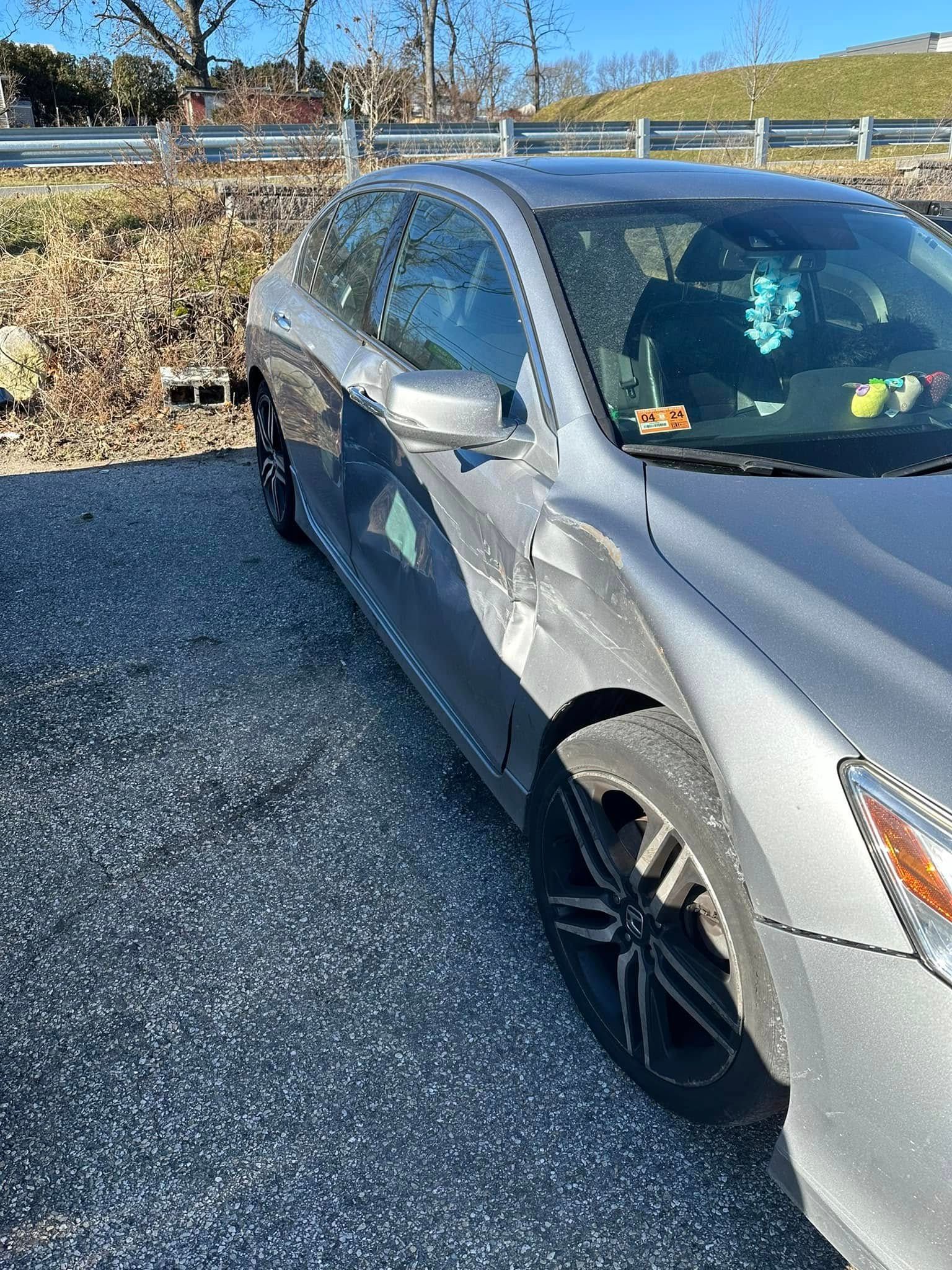 A silver car is parked on gravel in a parking lot.