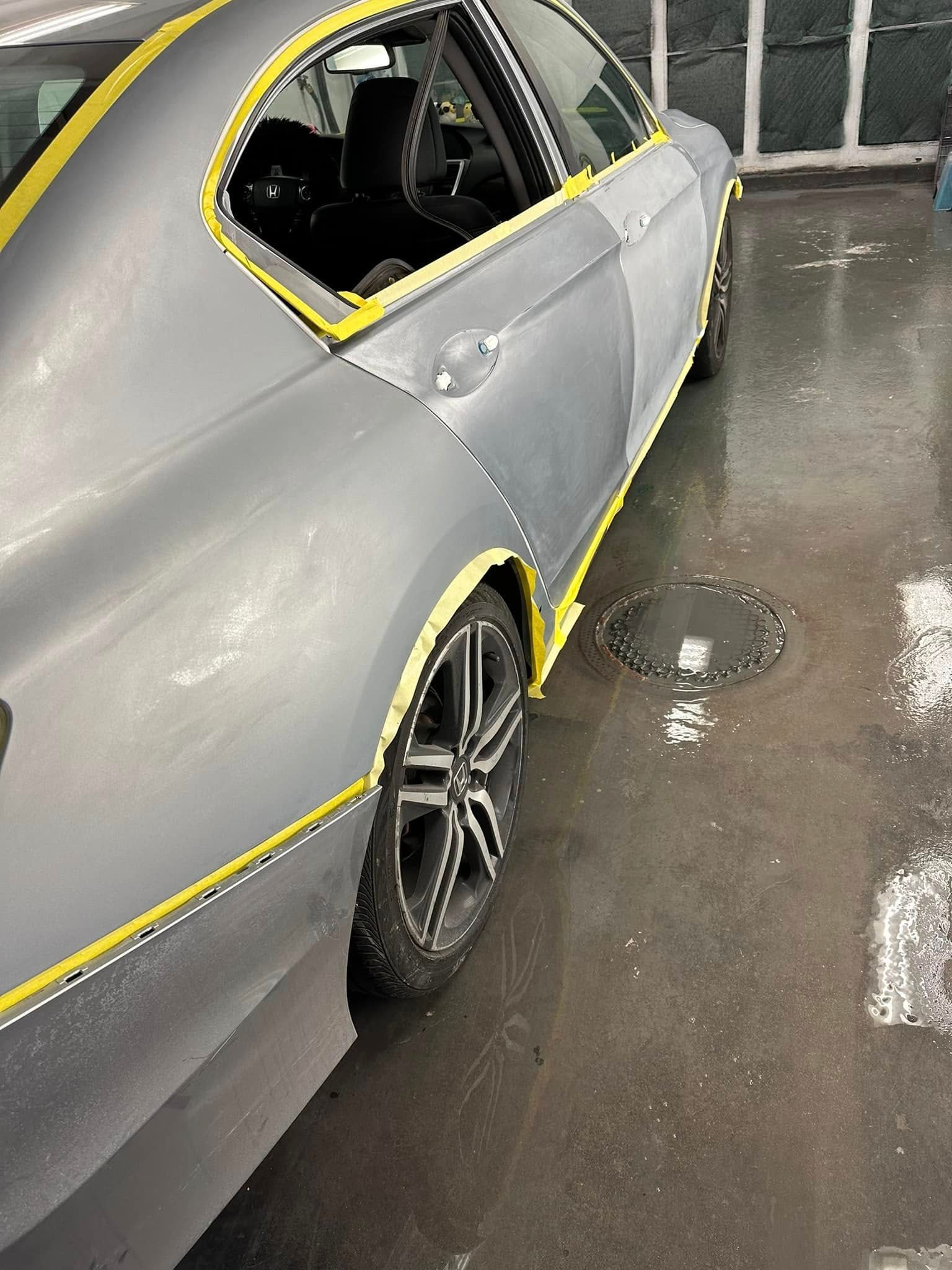 A gray car with yellow tape on the side is parked in a parking lot.