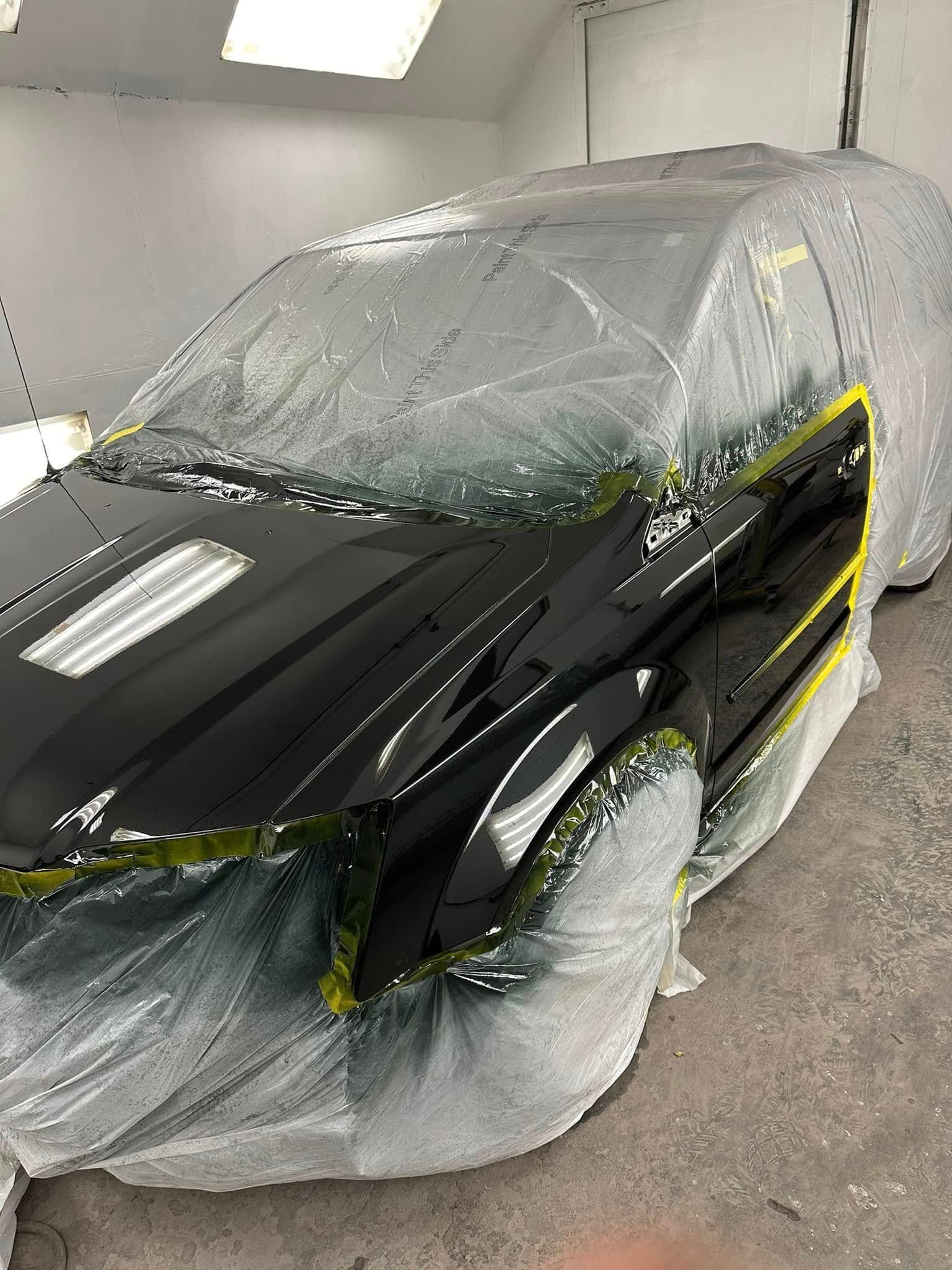 A black car is being painted in a paint booth.