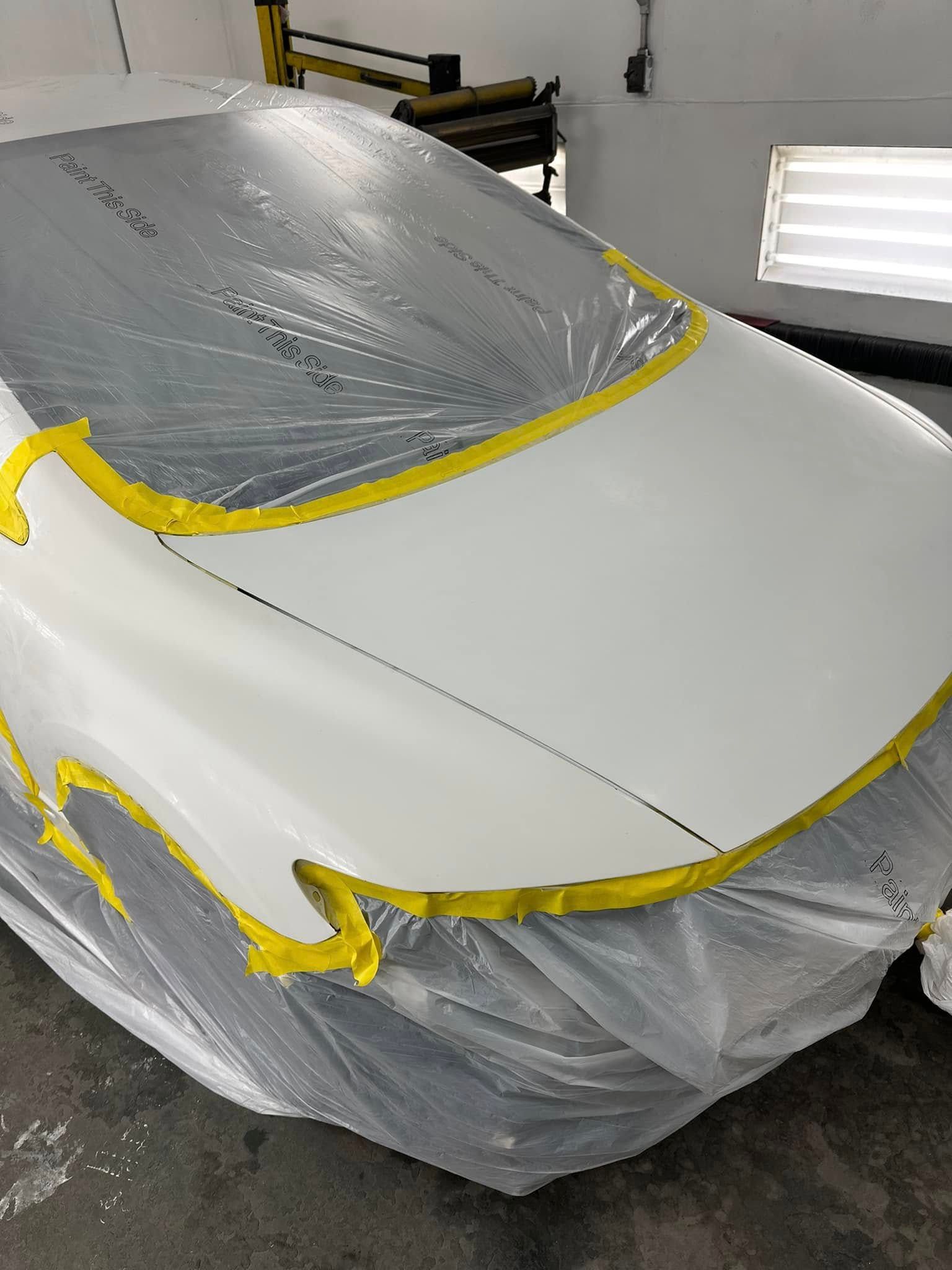 A white car is covered in plastic and yellow tape.
