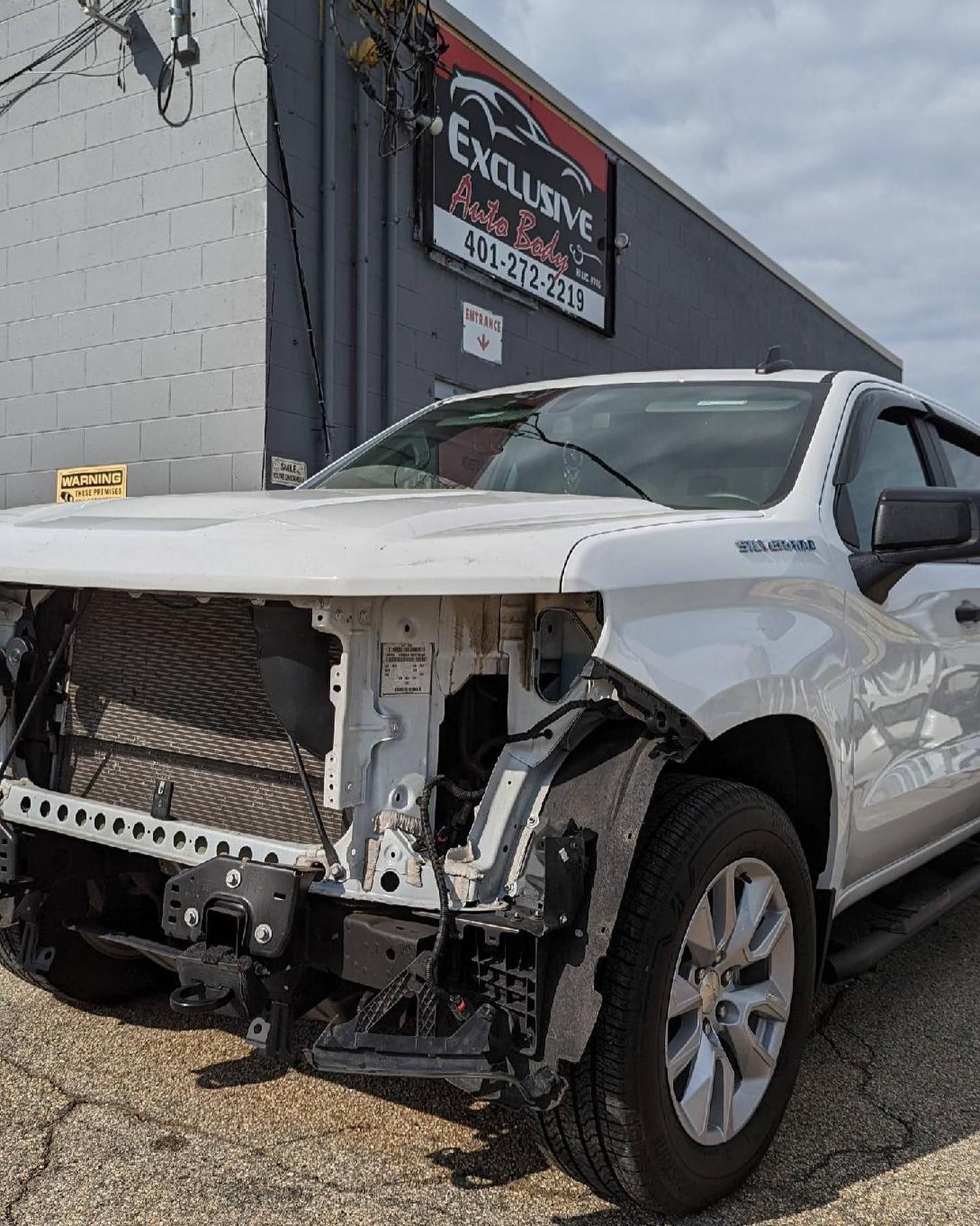 A white truck with a damaged front end is parked in front of a building.