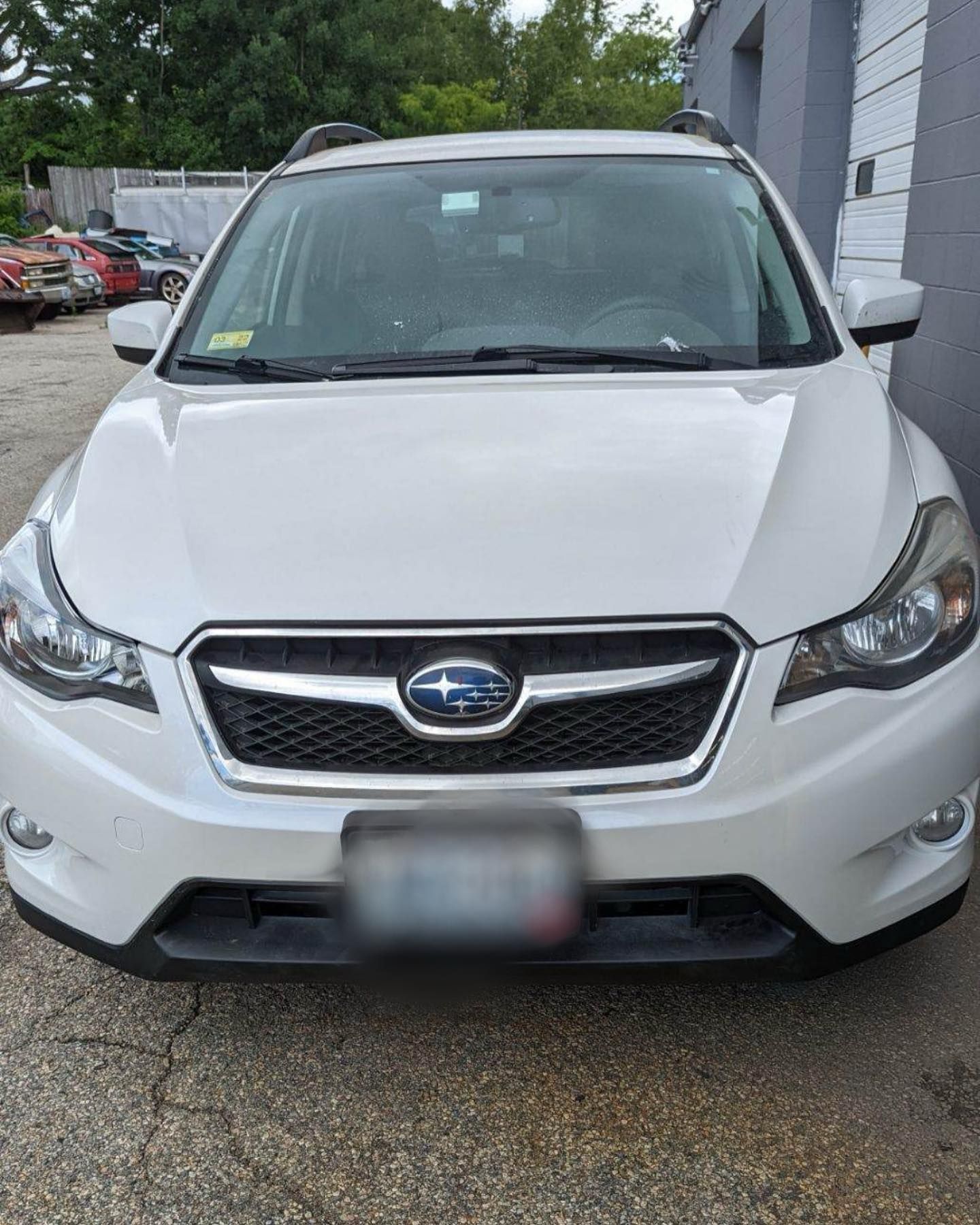 A white subaru is parked in a parking lot in front of a building.
